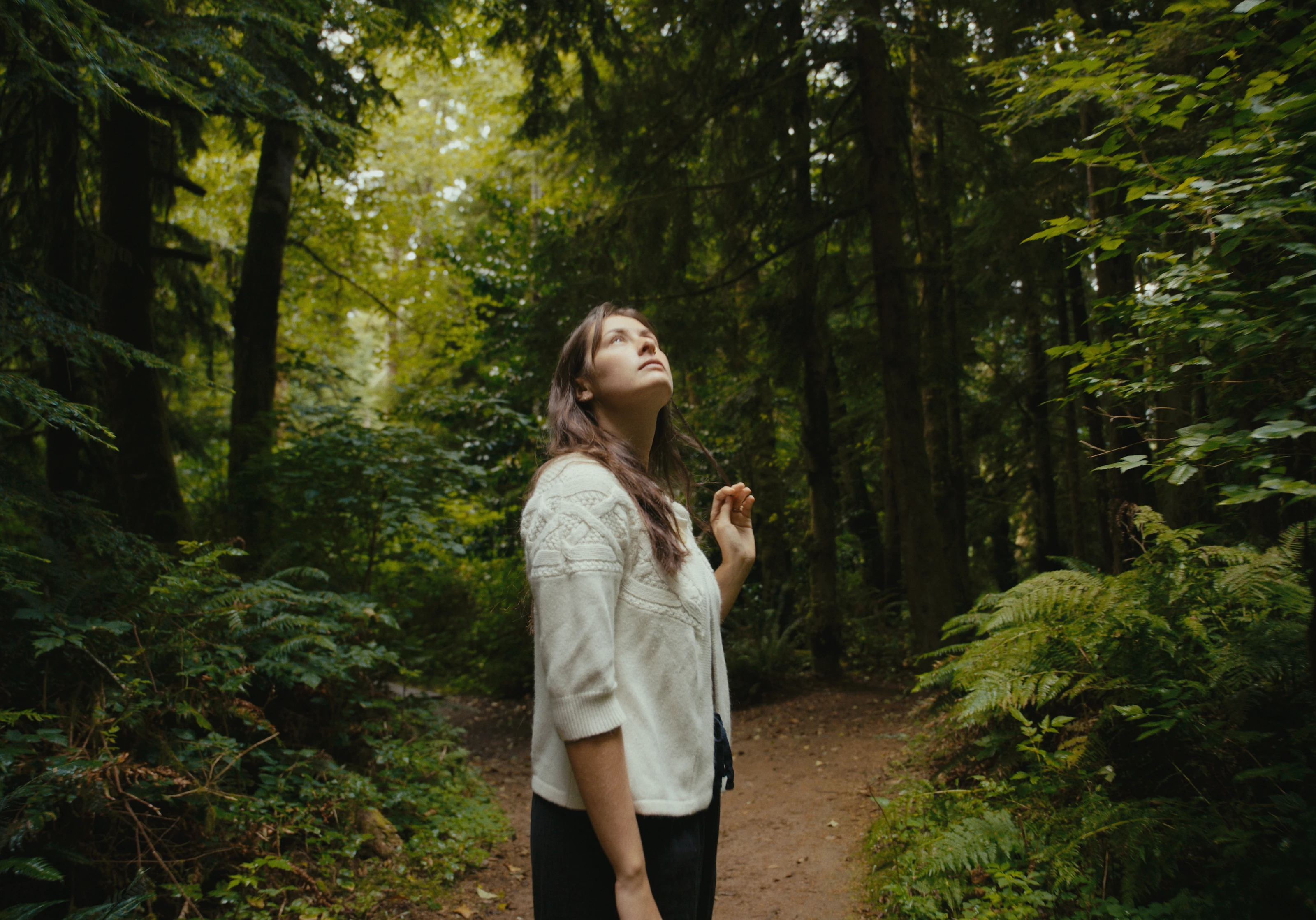 A woman looking upward among forest trees.