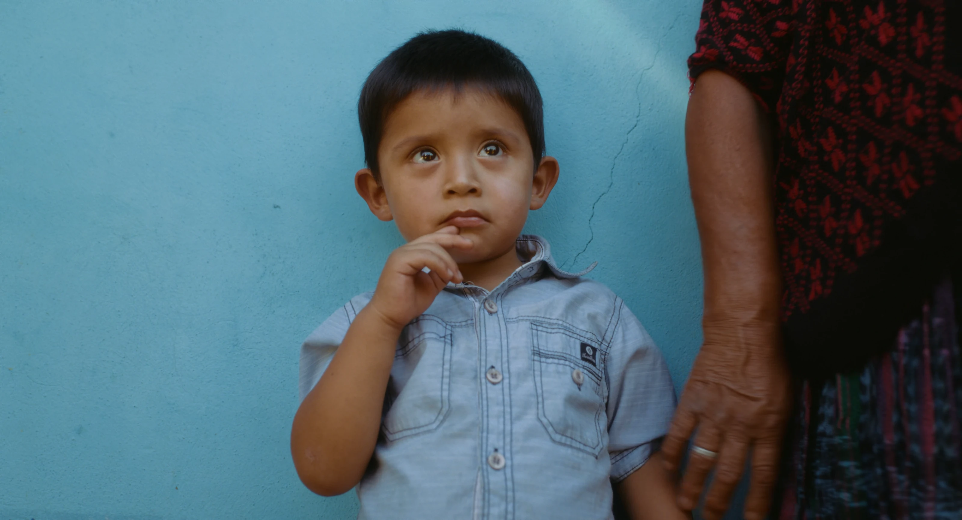 A child standing beside a blue wall in Guatemala.