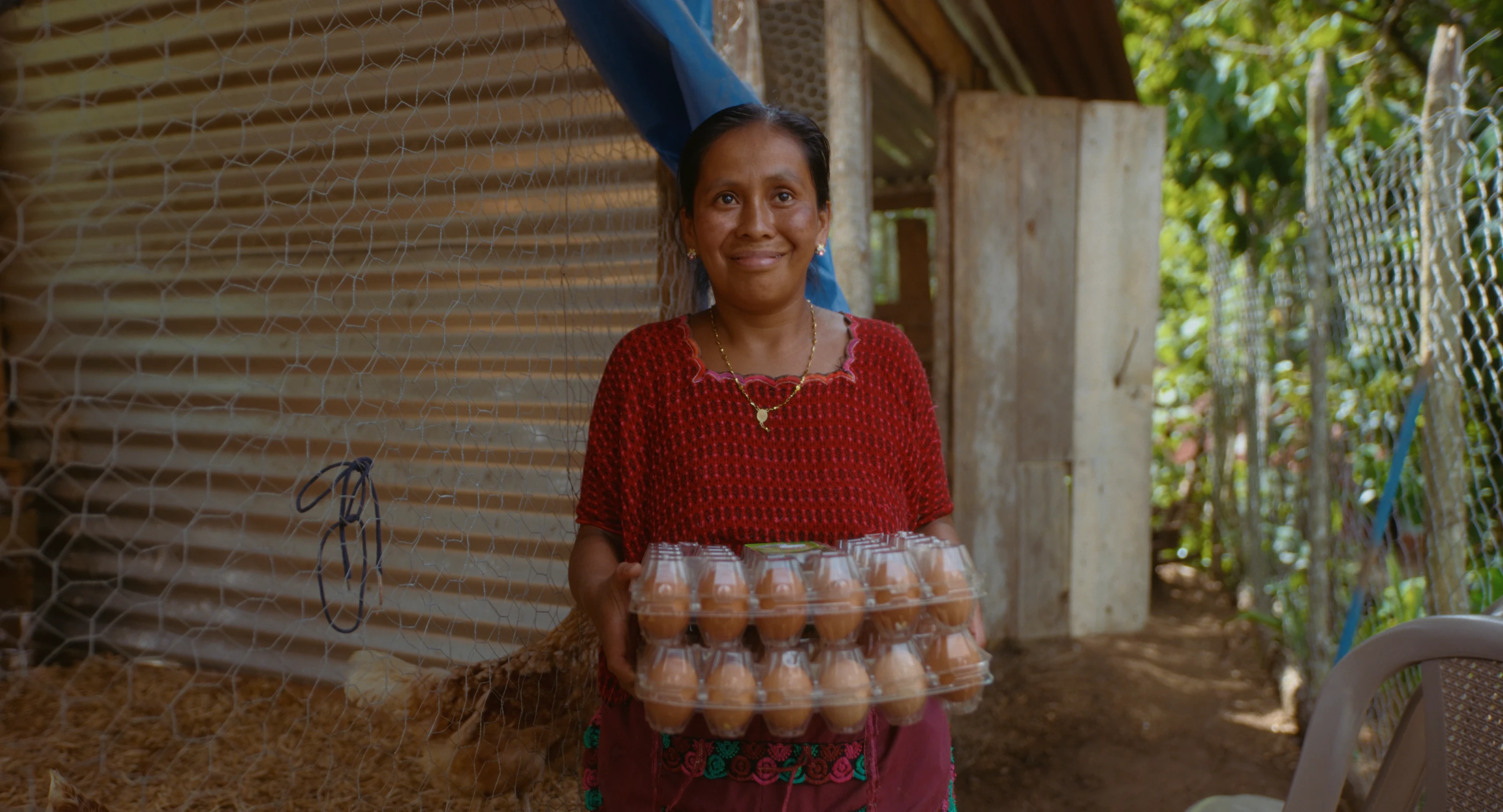 A woman holding egg trays beside a coop in Guatemala.