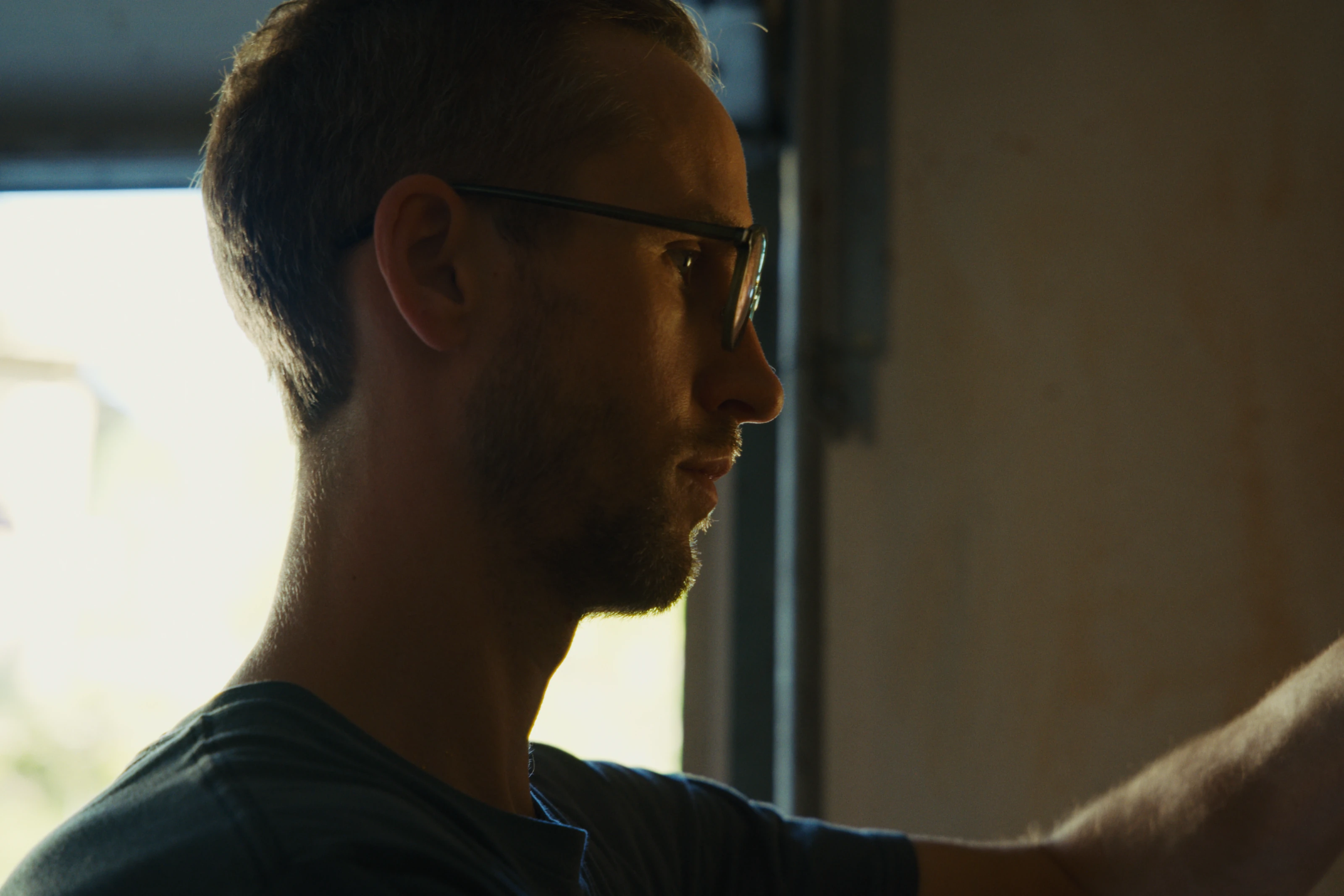 An artist in profile, working beside a sunlit window.